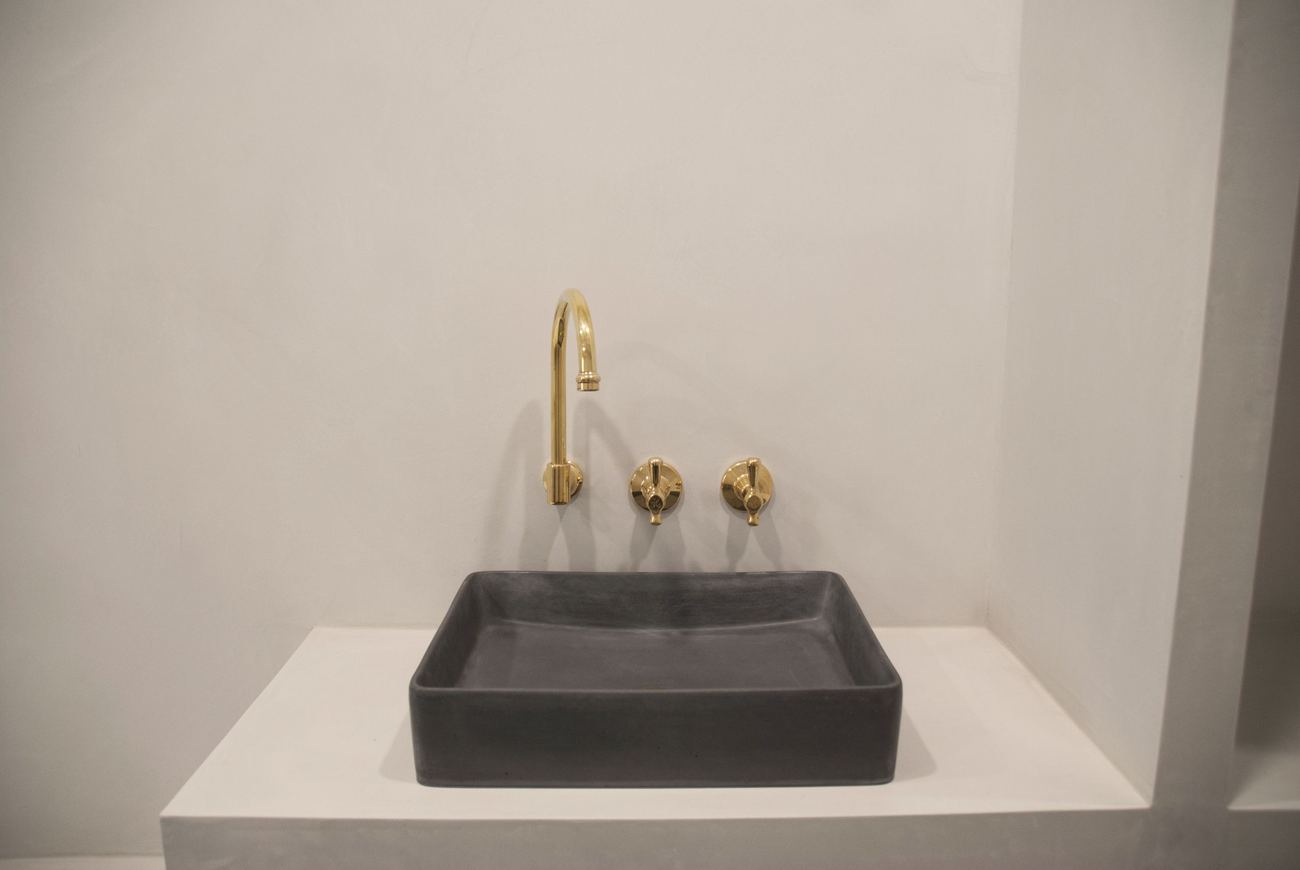 Microcement bathroom - hand-trowelled walls and a built-in vanity in one finish, with unlacquered brass taps and a black concrete basin